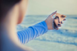 A woman looking at herself through a shard of a mirror.
